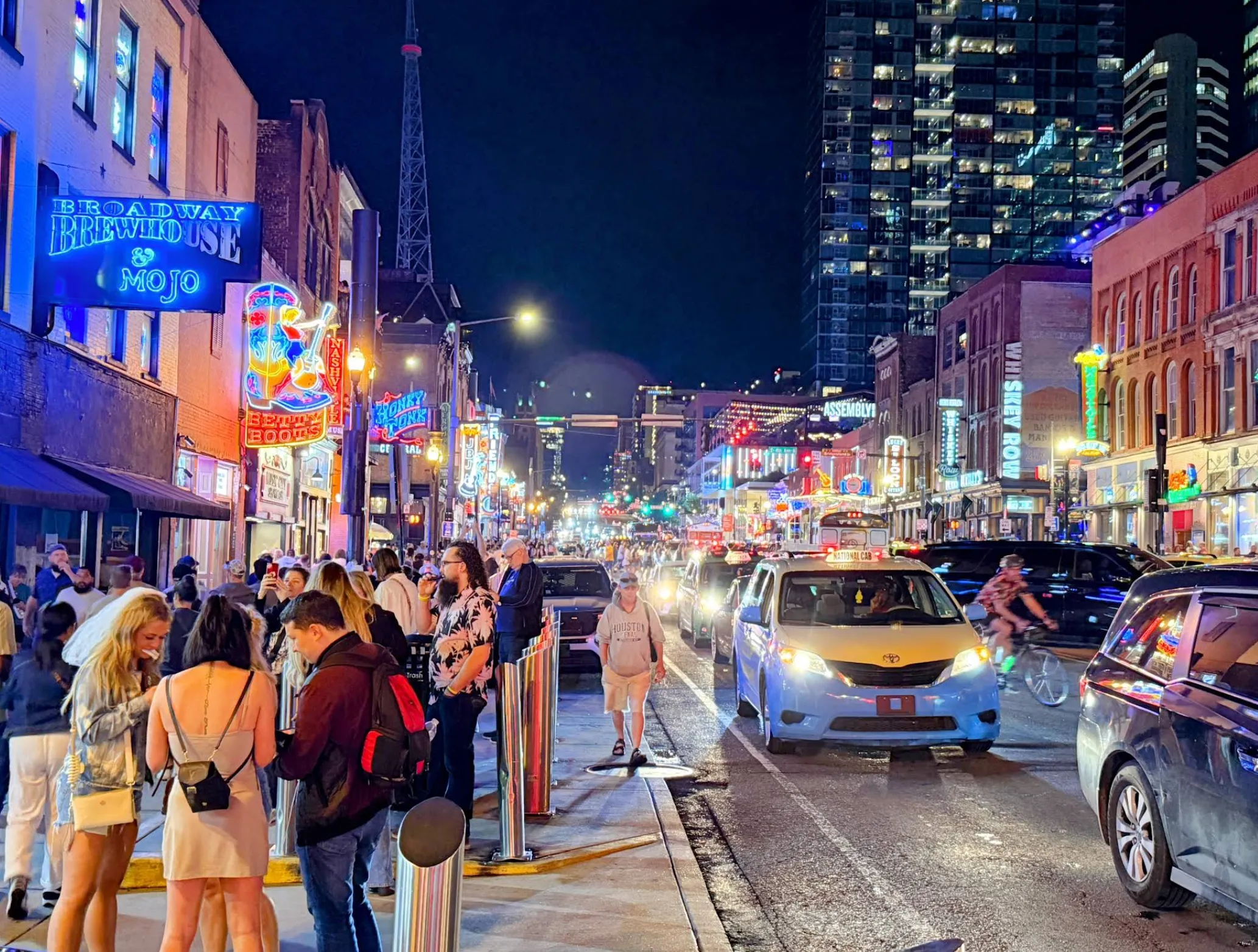 Image: A family walking along Broadway in daylight, neon signs and music venues in the background