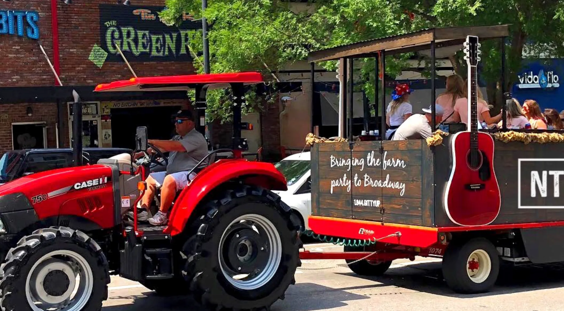 Image: A tractor-pulled party wagon driving past as a family watches from the sidewalk